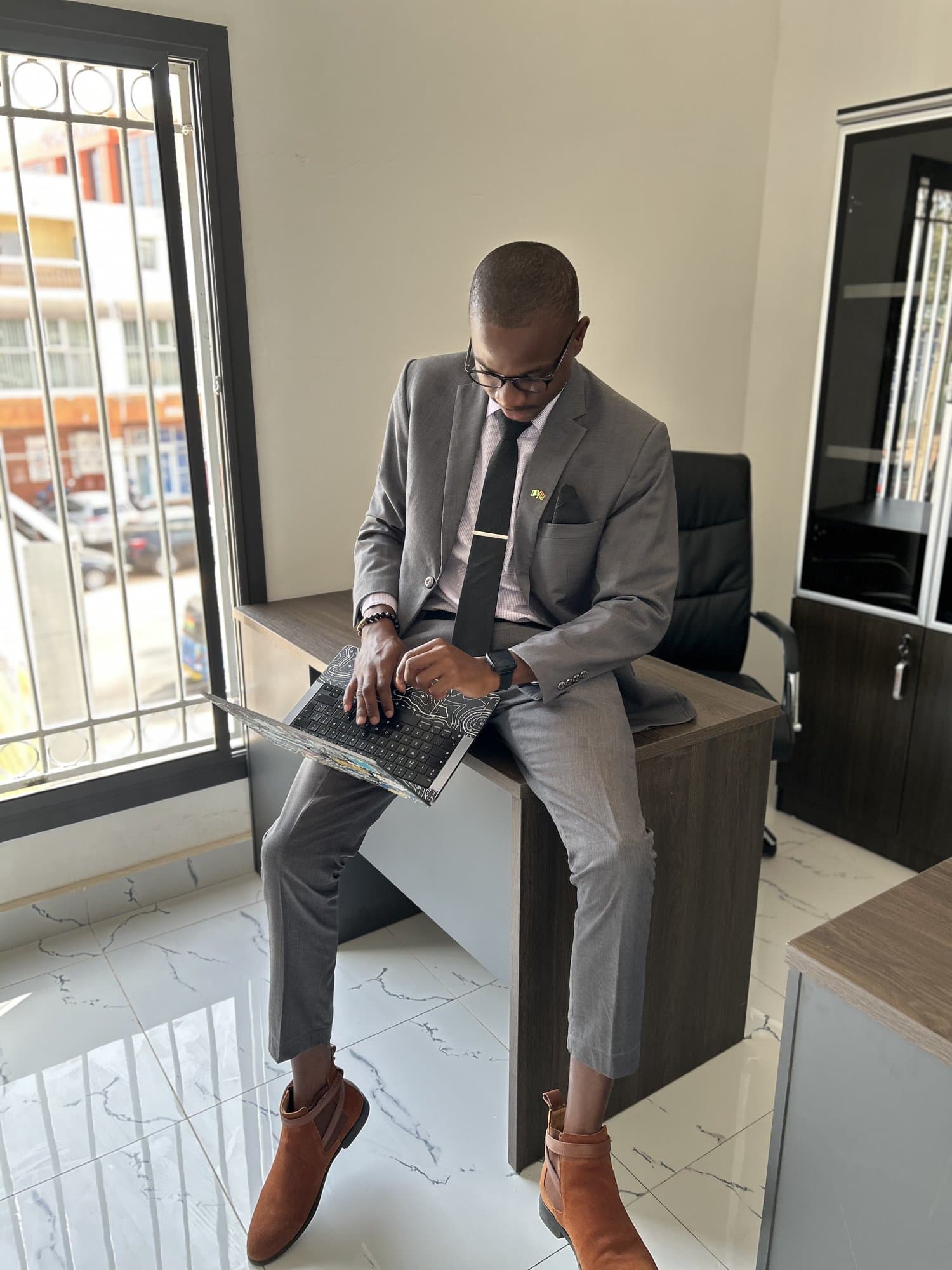 Jordan in a grey suit perched on an office desk